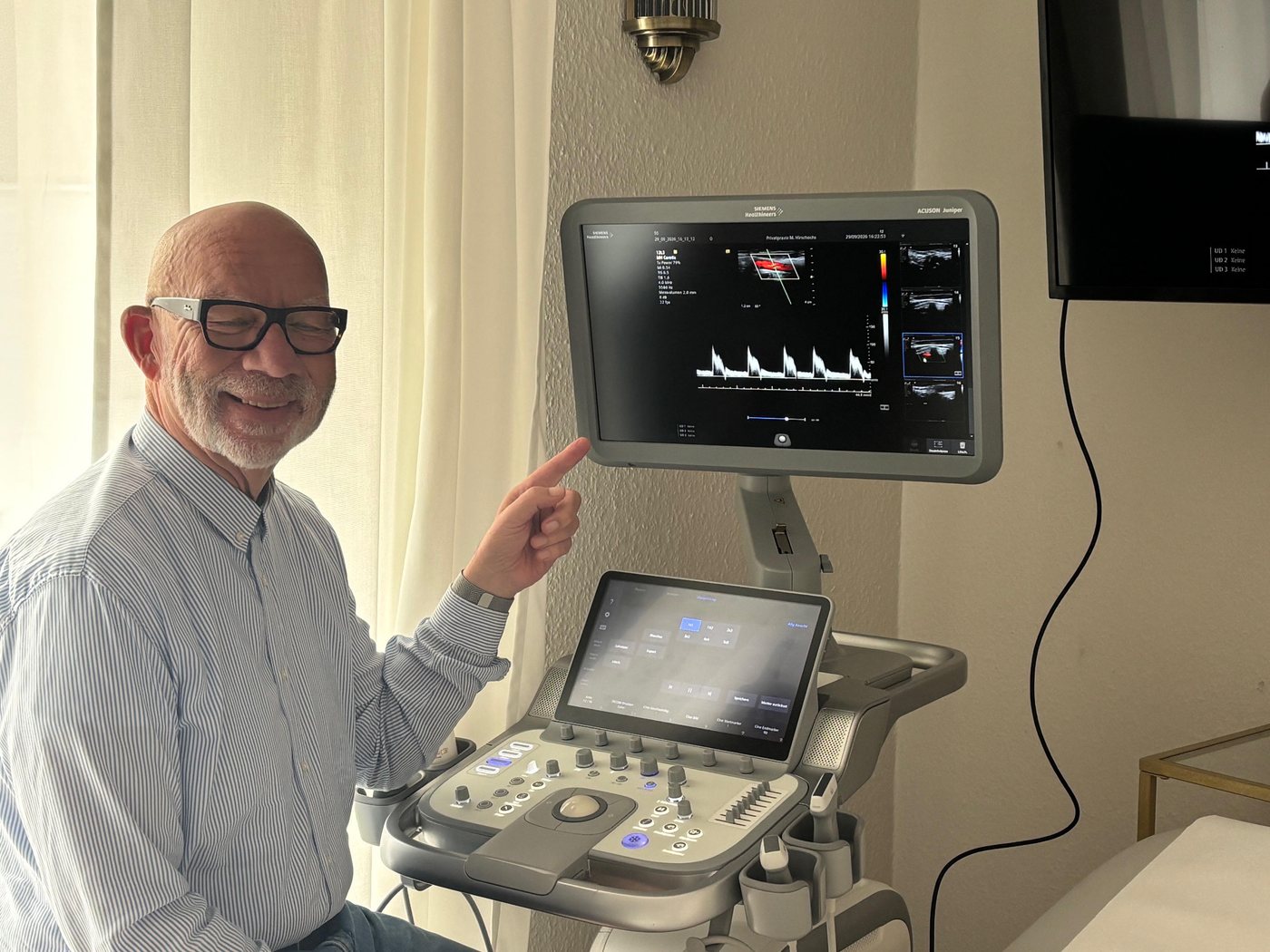 Manfred Hirschochs zeigt auf eine Aufnahme der Halsschlagader im Farbdoppler am Ultraschallgerät der Praxis