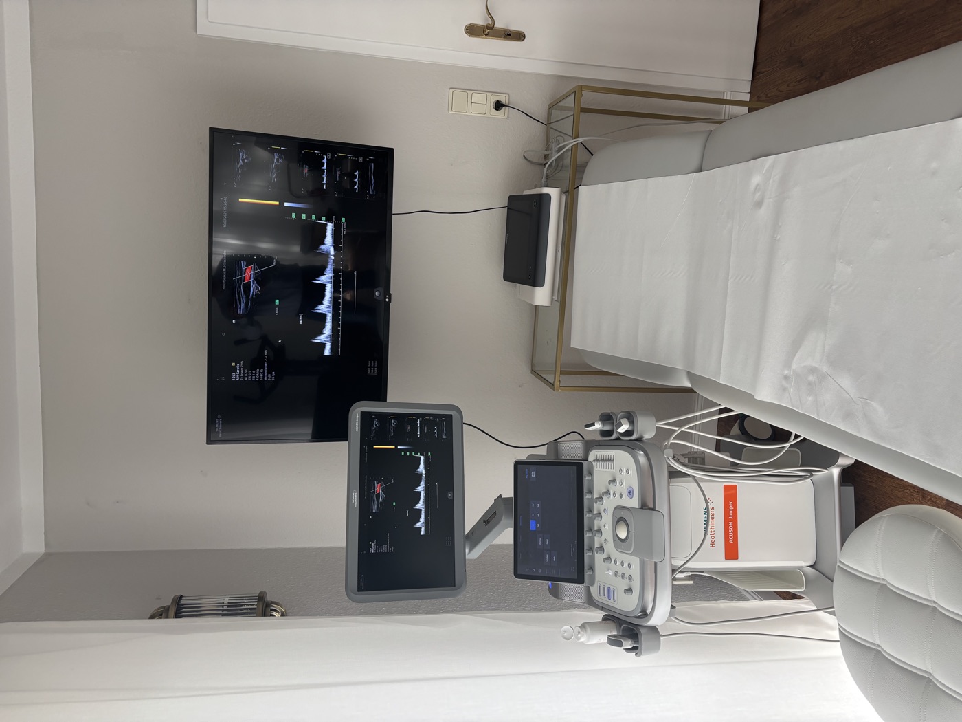 Ultraschallplatz der Praxis mit Liege, Ultraschallgerät und großem Bildschirm an der Wand